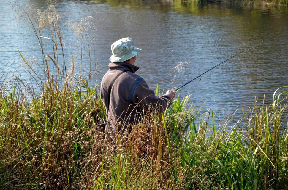 Free Image of A fisherman stands on the shore in a thicket of grass   