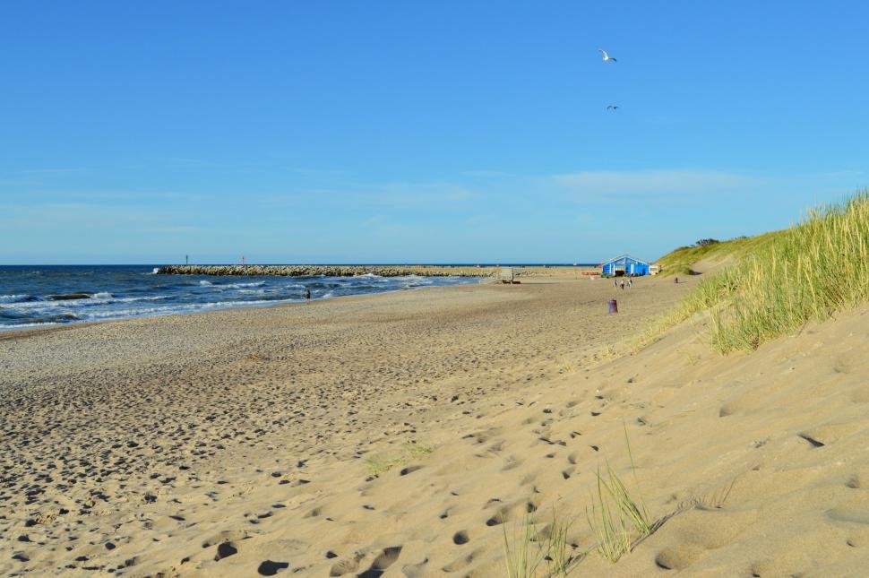 Free Image of Sandy coast of the Baltic Sea with a stone breakwater and the entrance to the harbor in the background 