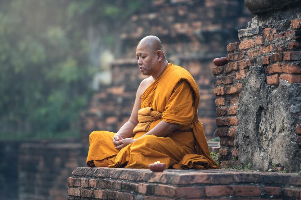Free Image of Man in Yellow Robe Sitting on Brick Wall 
