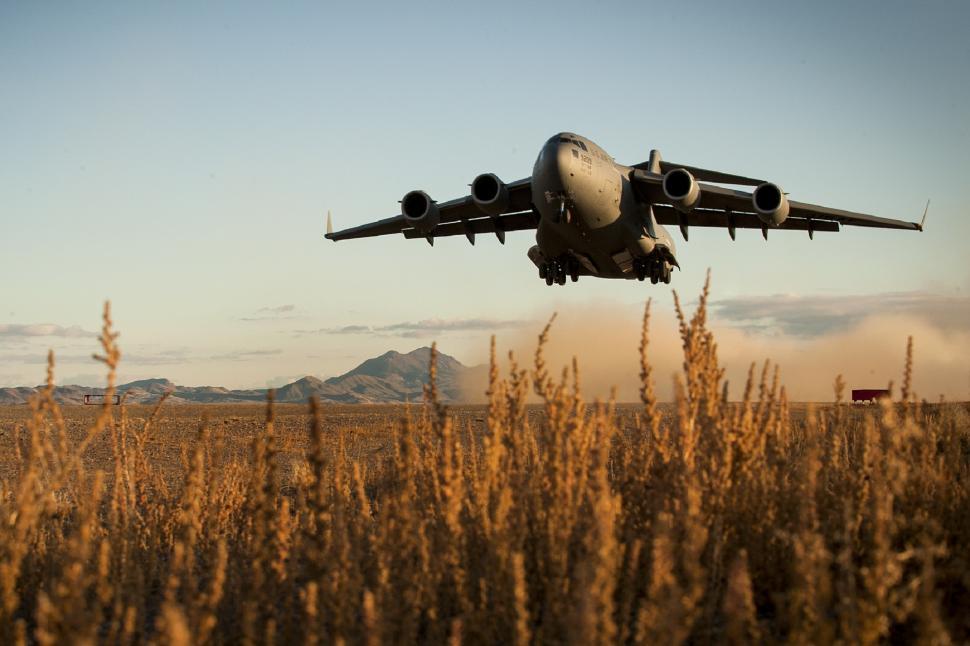 Free Image of Large Jetliner Flying Over Field of Tall Grass 