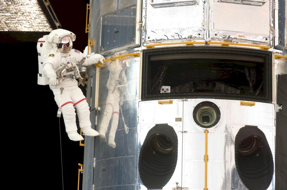 Free Image of Astronaut Hanging From Side of Space Station 