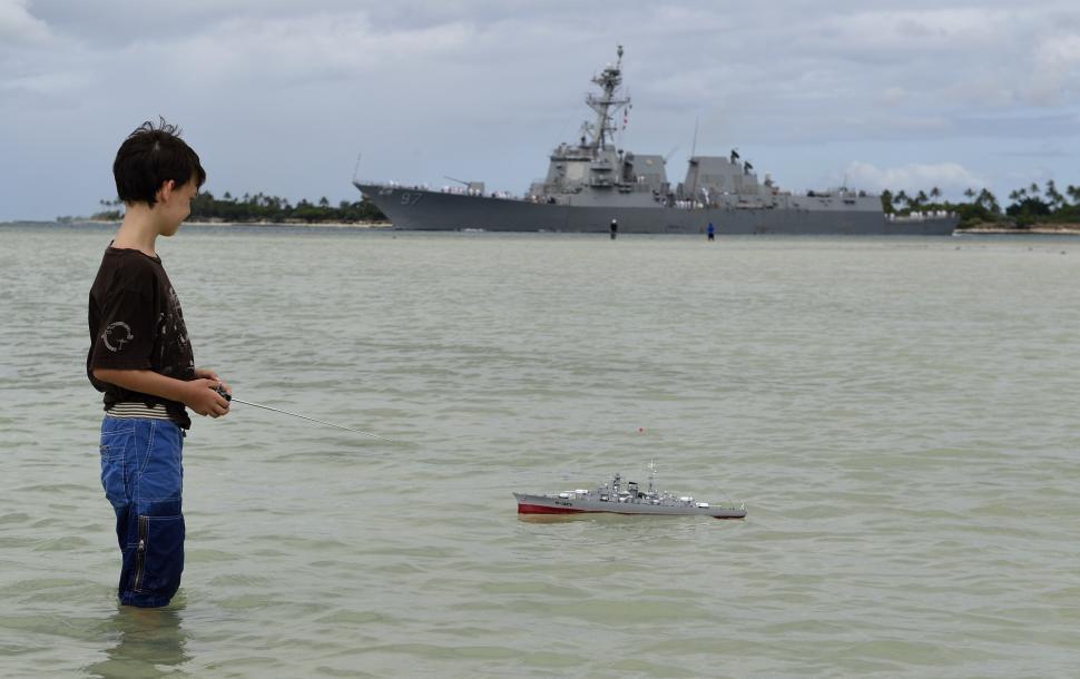 Free Image of Boy Standing in Water Looking at Toy Boat 