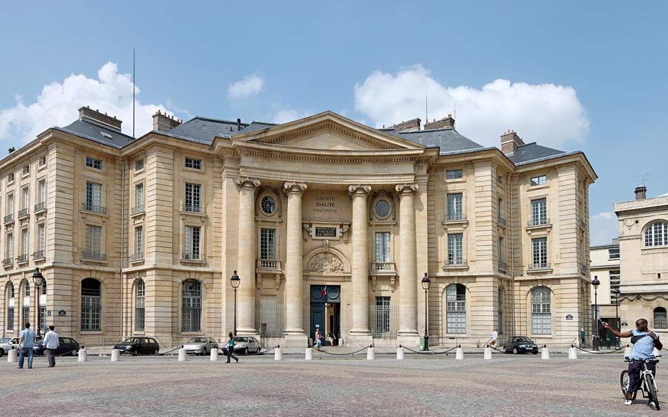 Free Image of Man Riding Bike in Front of Large Building 