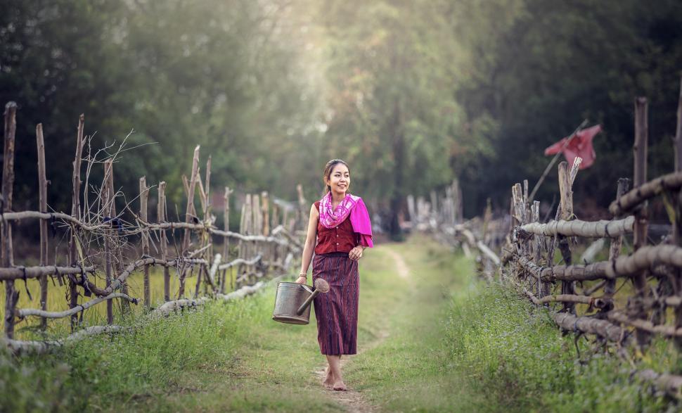 Free Image of Woman Walking Down Dirt Road Next to Lush Green Field 