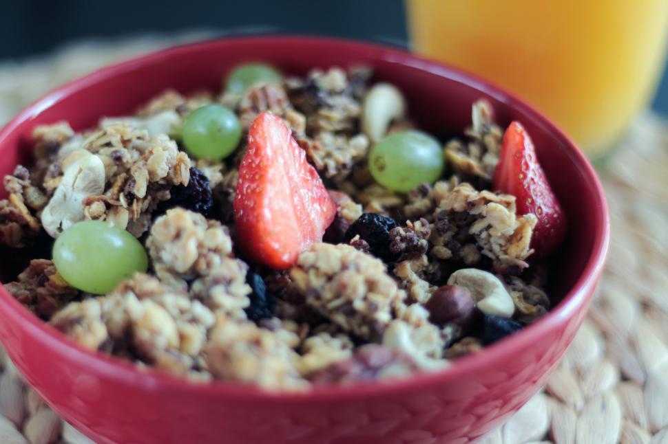 Free Image of Red Bowl With Cereal and Fruit Next to Glass of Orange Juice 