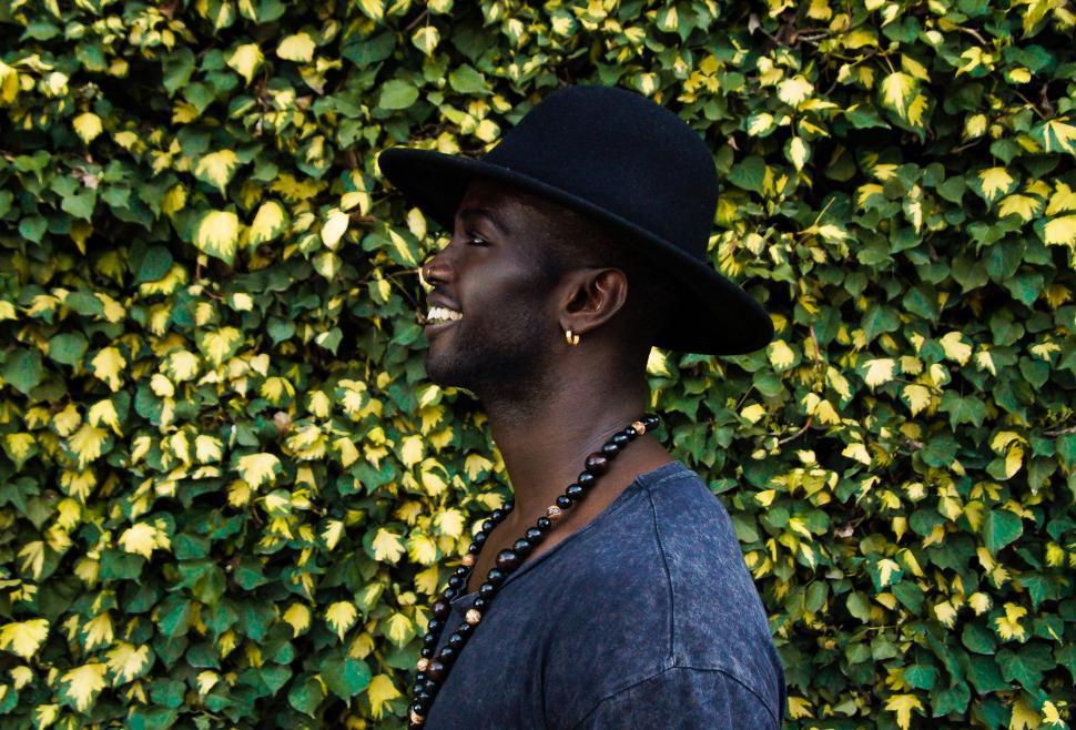 Free Image of Man in Black Hat Standing in Front of Green Wall 