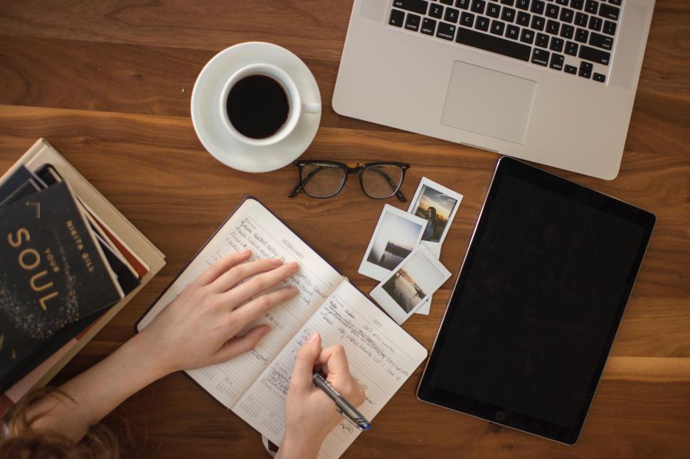 Free Image of Person Writing on Book Next to Laptop 