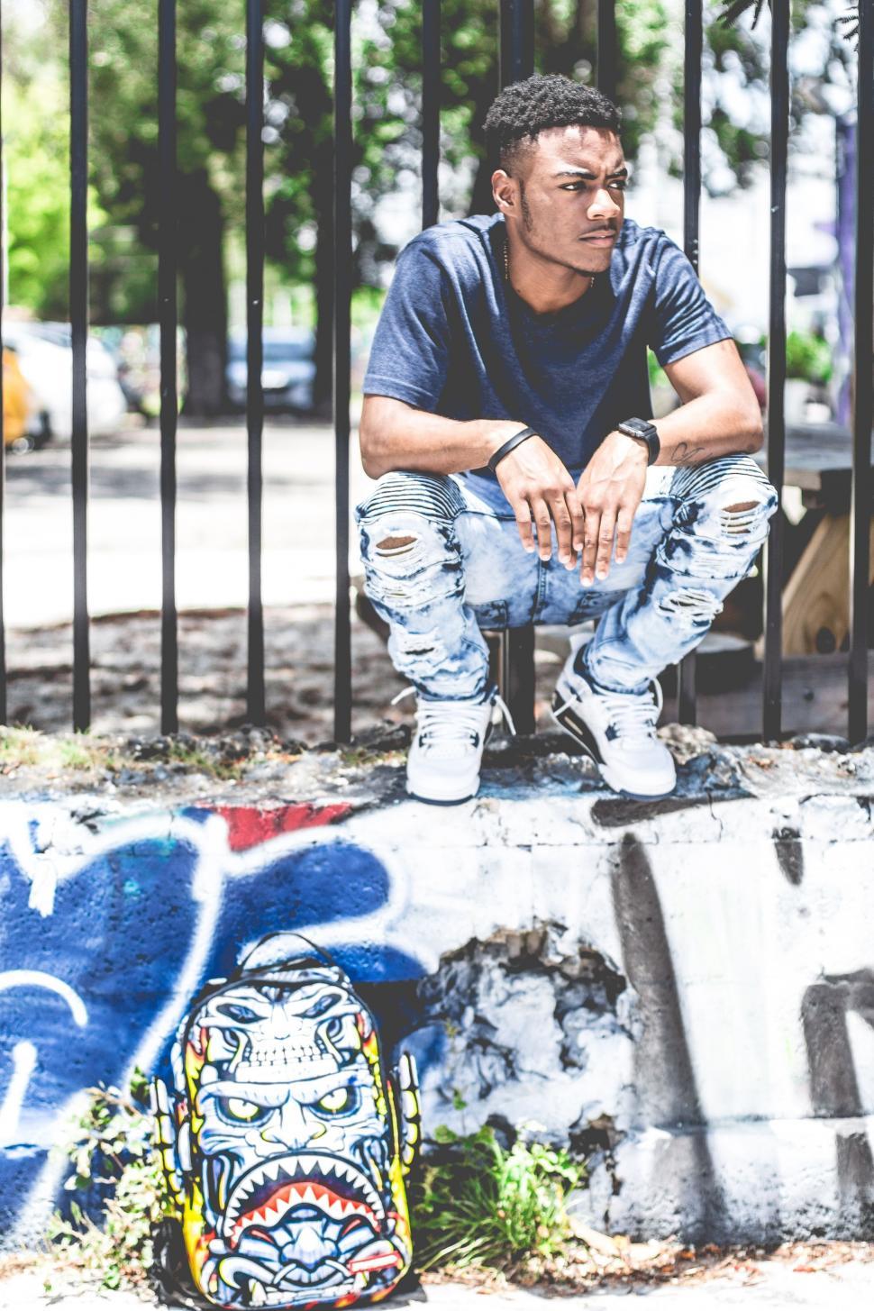 Free Image of Man Sitting on Wall With Backpack 