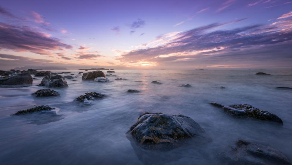 Free Image of Sun Setting Over Ocean With Rocks in Foreground 