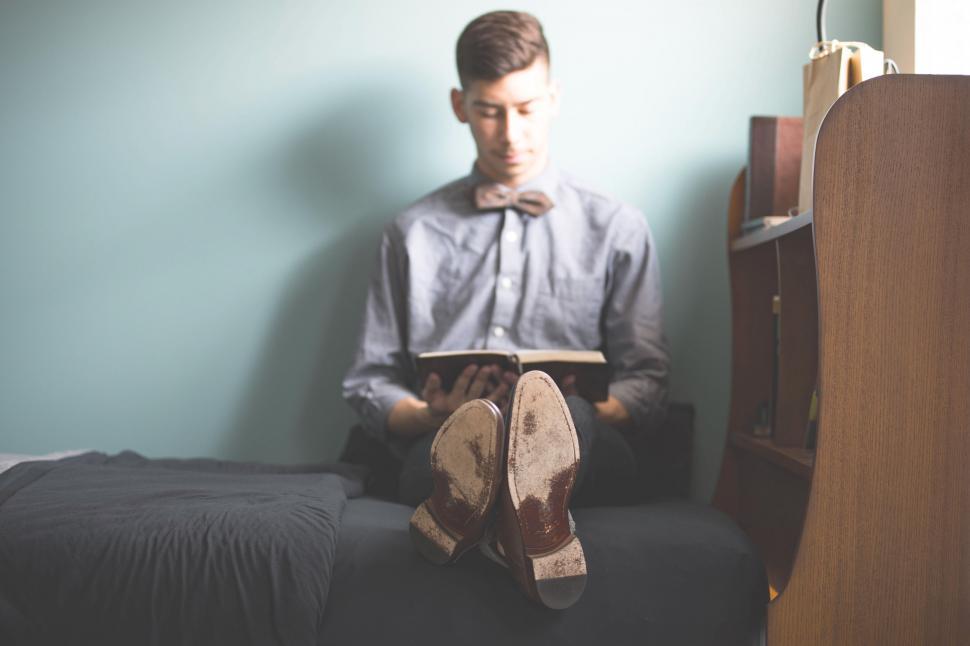 Free Image of Young Man Reading Book on Bed 