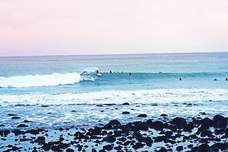 Free Image of Group of People Riding Waves on Top of a Surfboard 