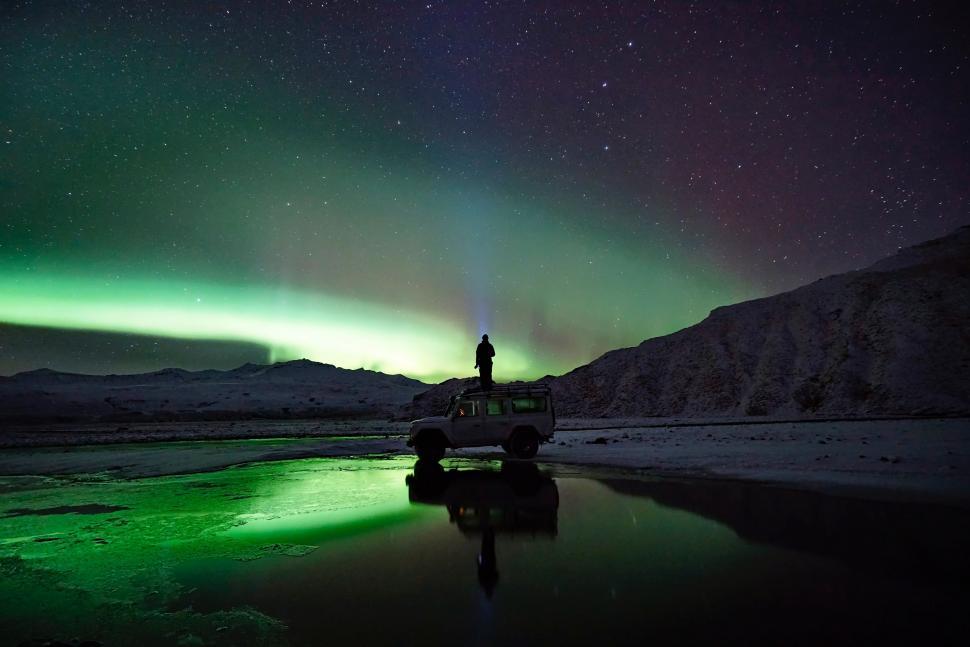 Free Image of Person Standing on Shore of Body of Water Under Green and Purple Sky 