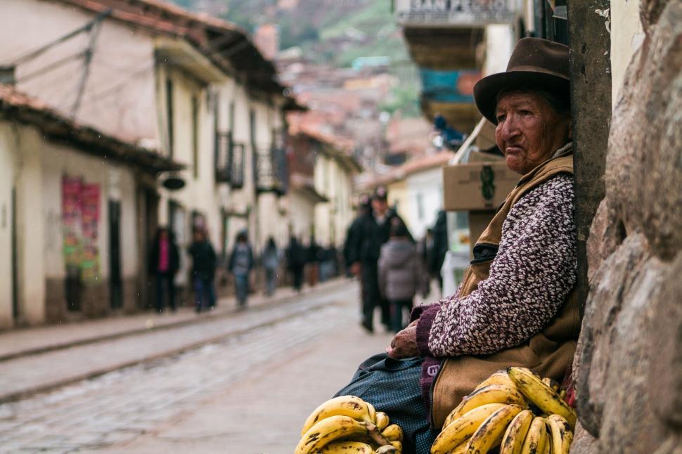 Free Image of Man Sitting on Wall With Bunch of Bananas 