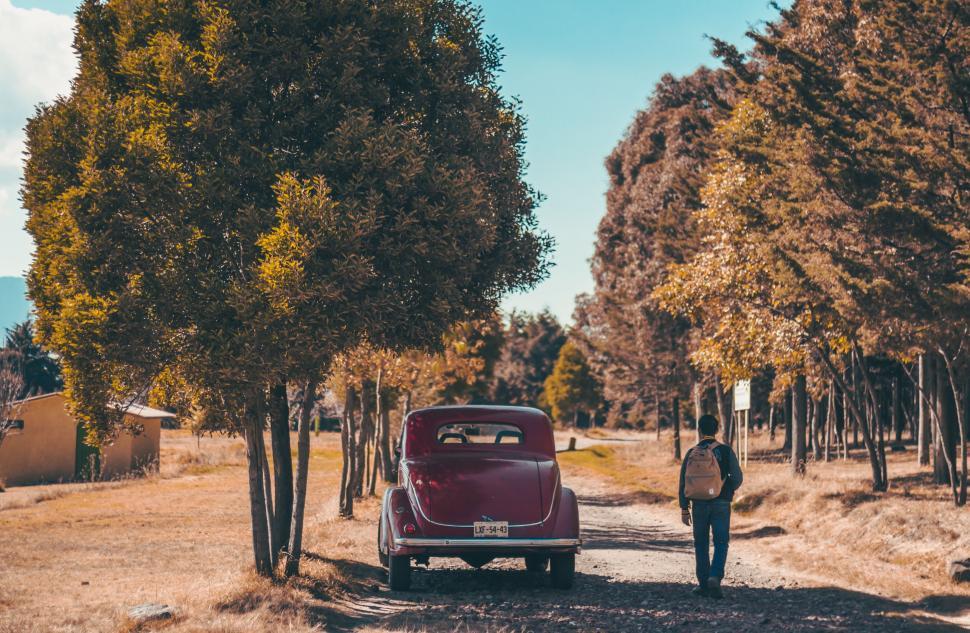 Free Image of Man Walking Down Dirt Road Next to Red Car 