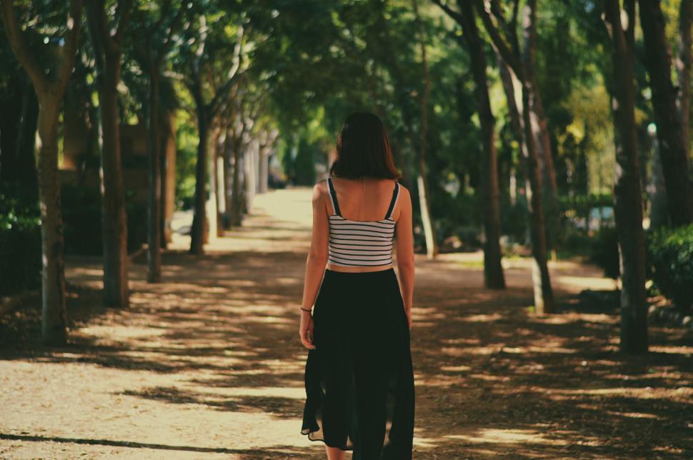 Free Image of Woman Walking Down a Tree Lined Path 