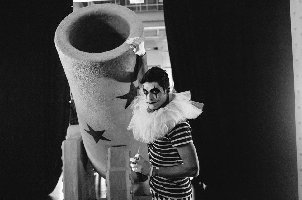 Free Image of Woman in Clown Makeup Standing Next to Large Vase 